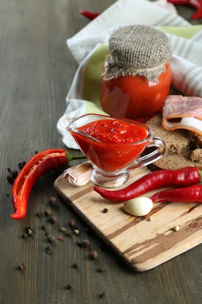 Composición con salsa sobre pan, ají rojo picante y ajo, sobre servilleta, sobre fondo de madera — Foto de Stock