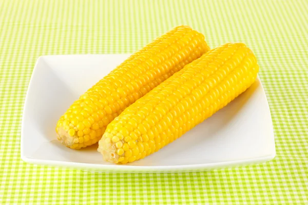 Boiled corn on the white plate on a green tablecloth — Stock Photo, Image