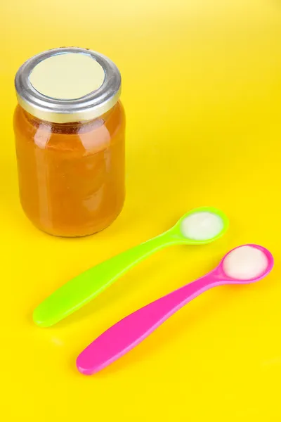 Color spoons for baby food with baby nutrition on yellow background — Stock Photo, Image