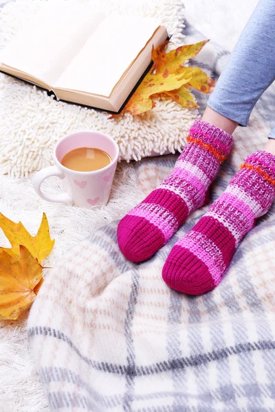 Composizione con plaid caldo, libro, tazza di bevanda calda e gambe femminili, su sfondo tappeto di colore — Foto Stock