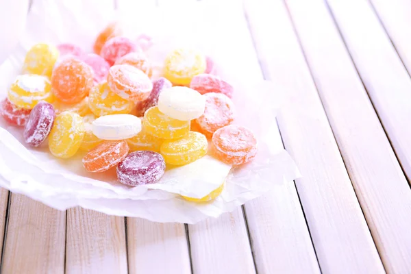 Sweet multicolor candies on paper, on color wooden background — Stock Photo, Image