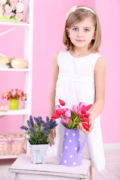 Vackra lilla tjej och stå med blommor på rosa bakgrund — Stockfoto