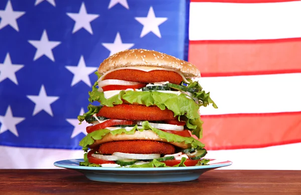 Huge burger on color plate on USA flag background — Stock Photo, Image