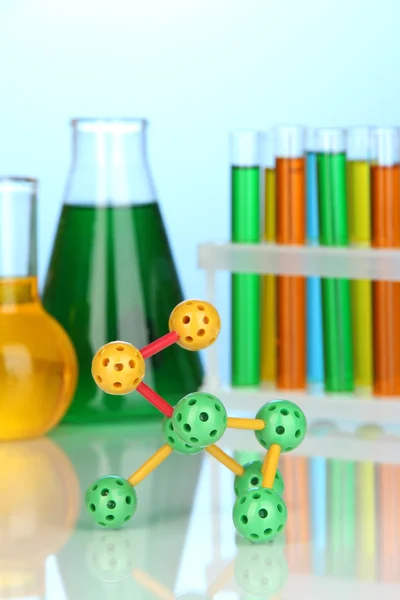 Molekülmodell und Reagenzgläser mit bunten Flüssigkeiten auf blauem Hintergrund — Stockfoto