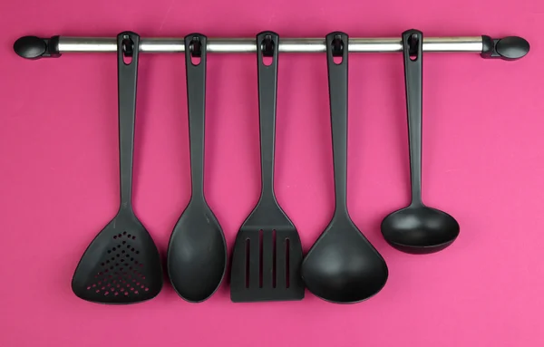 Plastic kitchen utensils on silver hooks on red background — Stock Photo, Image