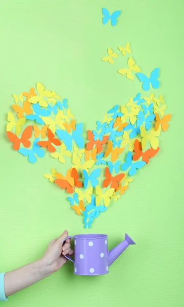 Paper butterflies fly out of watering can on green wall background — Stock Photo, Image