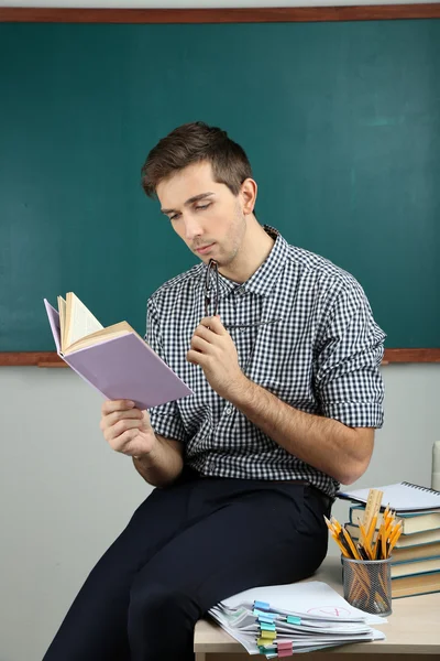 Young teacher sitting on desk in school classroom — Stock Photo, Image