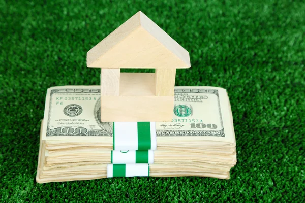 Wooden house on packs of dollars on grass close-up — Stock Photo, Image