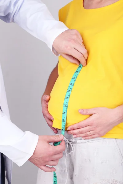 Mujer embarazada joven con médico sobre fondo gris — Foto de Stock