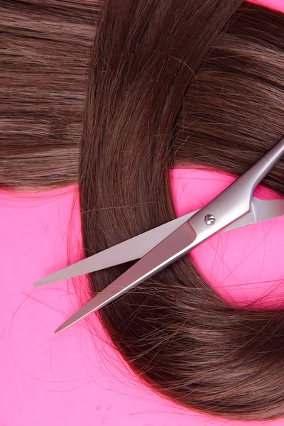 Lunghi capelli castani con forbici su sfondo rosa — Foto Stock