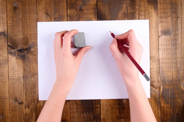 Manos sosteniendo lápiz y borrar con papel sobre fondo de madera — Foto de Stock