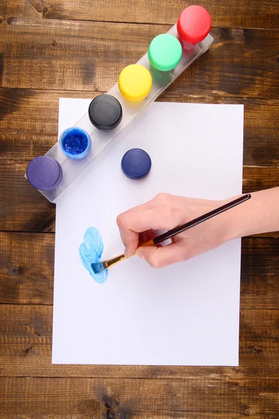 Ręka trzyma pędzel z farby i papieru na drewniane tła — Zdjęcie stockowe
