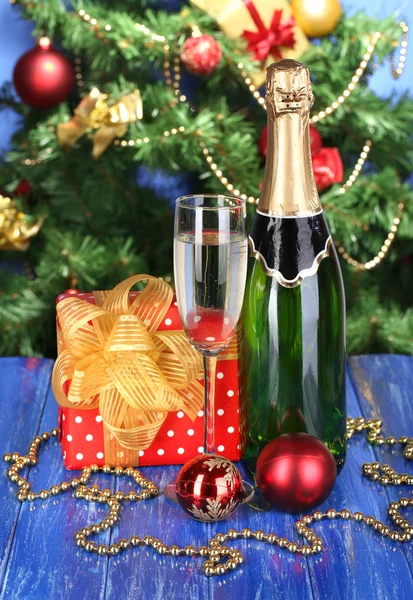 Bottle of champagne with glasses and Christmas balls on wooden table on Christmas tree background — Stock Photo, Image