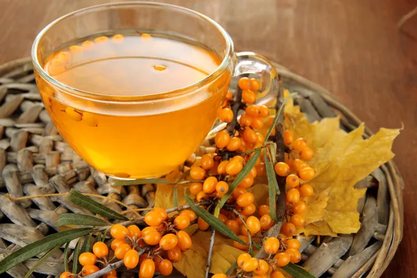 Branches of sea buckthorn with jam on wicker stand on wooden background — Stock Photo, Image