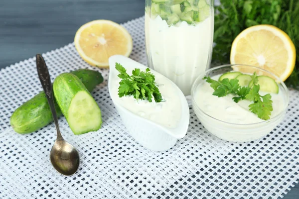 Komkommer yoghurt in glas en kom, op kleur servet,, op donkere houten achtergrond — Stockfoto