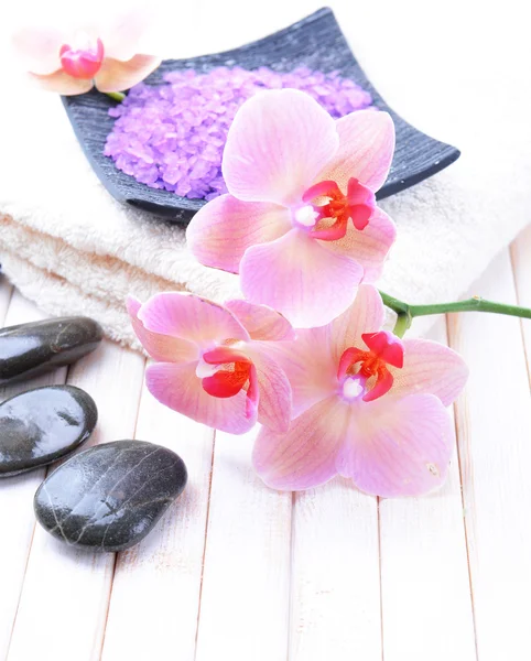 Still life with beautiful blooming orchid flower, towel and bowl with sea salt, on color wooden background — Stock Photo, Image