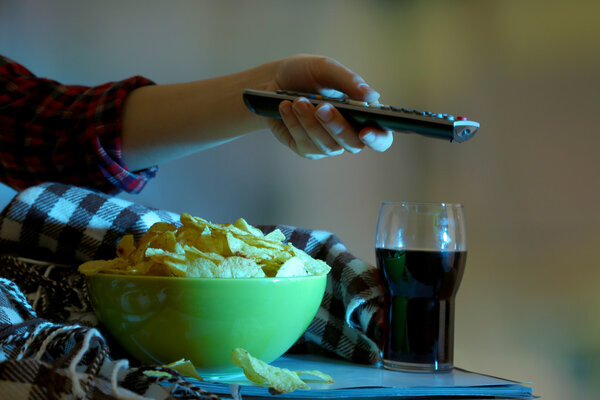 Кто-то смотрит телевизор с чипсами и колой в комнате
