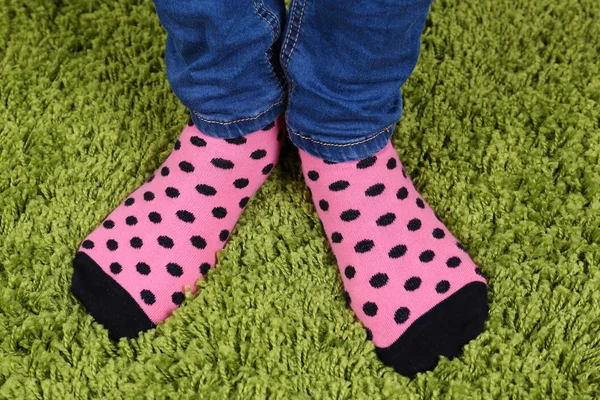 Female legs in blue jeans trousers and colorful socks on green carpet background — Stock Photo, Image