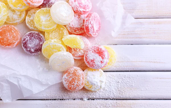 Dolci caramelle multicolore su carta, su sfondo di legno a colori — Foto Stock