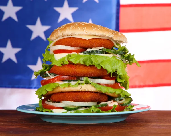 Burger enorme na placa de cor no fundo da bandeira dos EUA — Fotografia de Stock