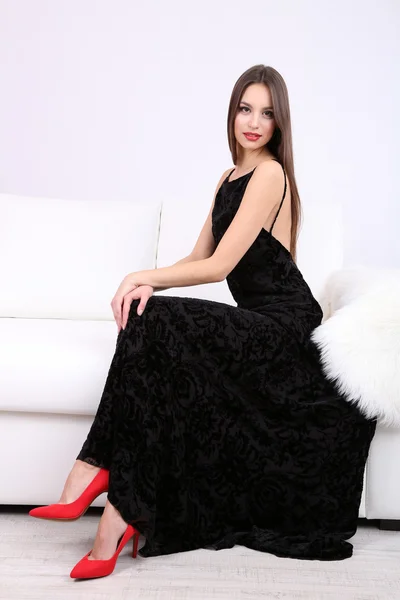 Piękna młoda kobieta w czarnej sukience na kanapie na białym tle — Zdjęcie stockowe