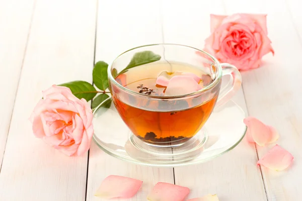 Φλιτζάνι τσάι με τριαντάφυλλα σε λευκό ξύλινο τραπέζι — Φωτογραφία Αρχείου