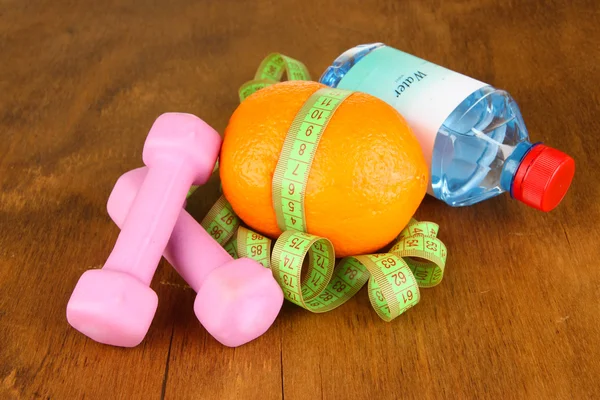 Orange with measuring tape,dumbbells and bottle of water, on wooden background — Stock Photo, Image