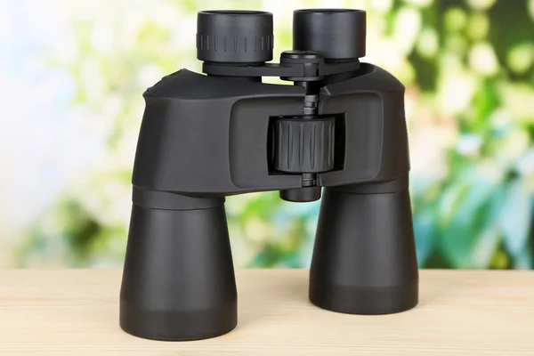 Black modern binoculars on wooden table on green background — Stock Photo, Image