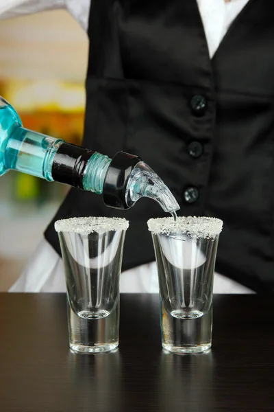 Barmen hand with bottle pouring beverage into glasses, on bright background — Stock Photo, Image