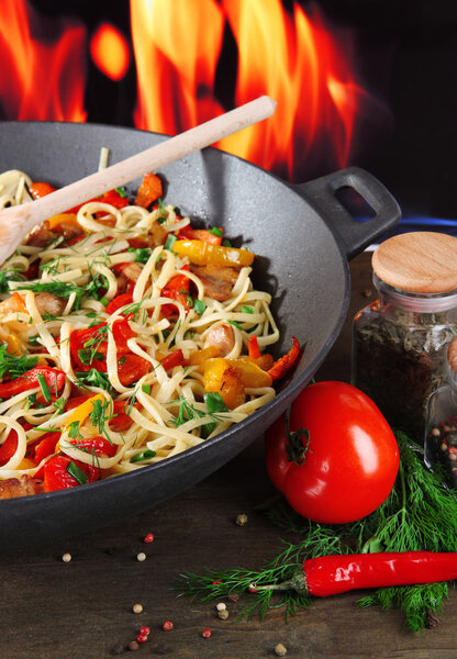 Noodles with vegetables on wok on fire background