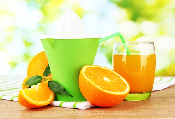 Citrus press, glass of juice and ripe oranges on brown wooden table — Stock Photo, Image