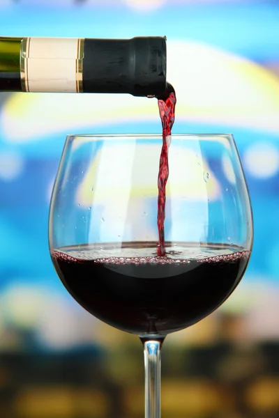 Vinho tinto sendo derramado em copo de vinho, em fundo brilhante — Fotografia de Stock
