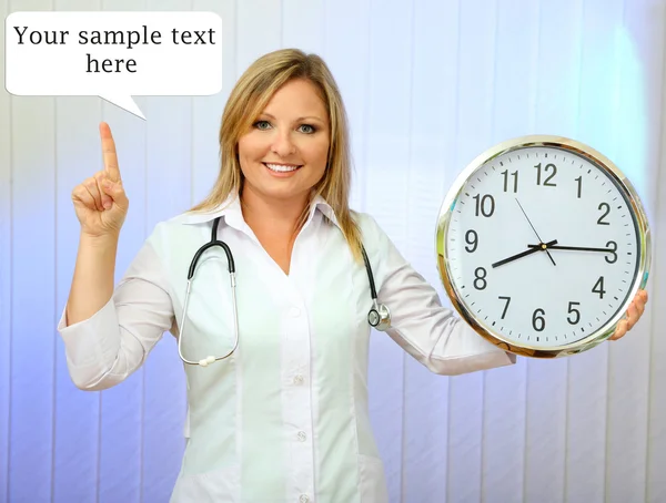 Young beautiful doctor with stethoscope and clock, on light background — Stock Photo, Image