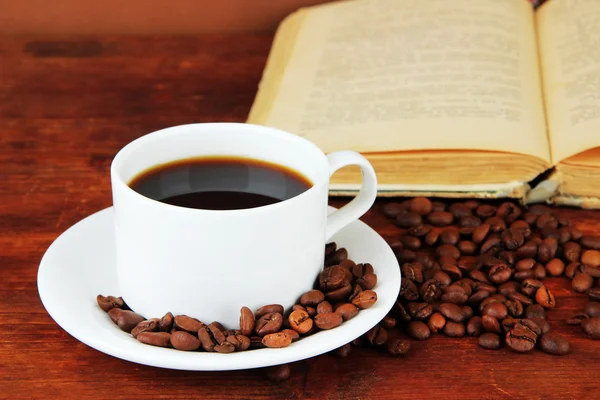 Kopp kaffe med kaffebönor och bok om trä bakgrund Stockbild