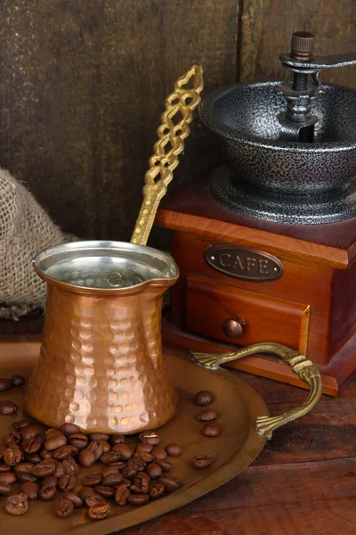 Koffiemolen, turk en koffie bonen op gouden lade op houten achtergrond — Stockfoto