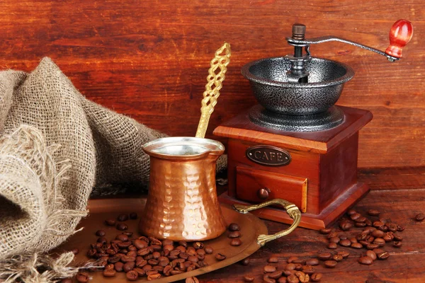 Koffiemolen, turk en koffie bonen op gouden lade op houten achtergrond — Stockfoto
