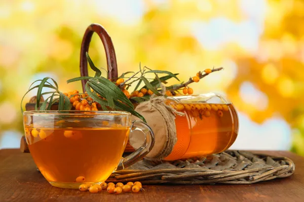 Branches of sea buckthorn with tea and jam on table on bright background — Stock Photo, Image