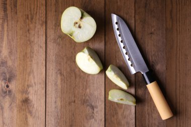 Mutfak bıçağı ve yeşil elma, ahşap arka planda.