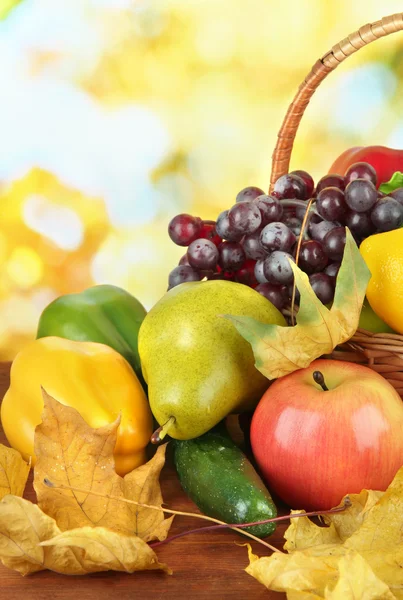 Frutas e legumes diferentes com folhas amarelas na cesta na mesa no fundo brilhante — Fotografia de Stock