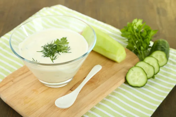 Yogur de pepino en un tazón de vidrio, en una servilleta de color, sobre un fondo de madera —  Fotos de Stock