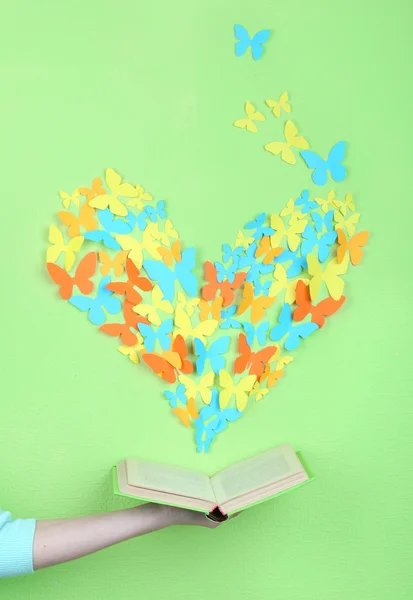 Paper butterflies fly out of book on green wall background — Stock Photo, Image