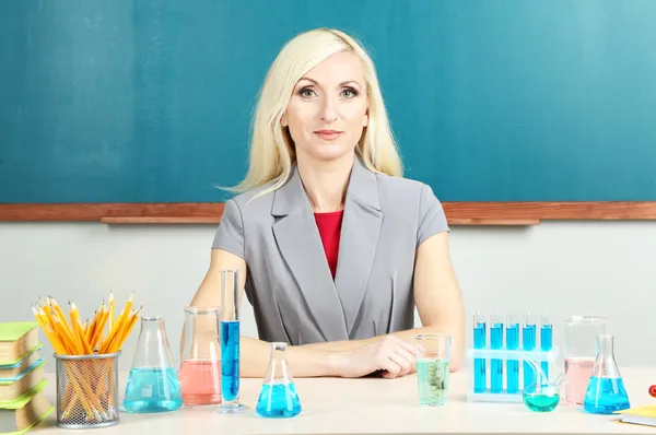 Scheikunde leraar zittend aan tafel op blackboard achtergrond — Stockfoto