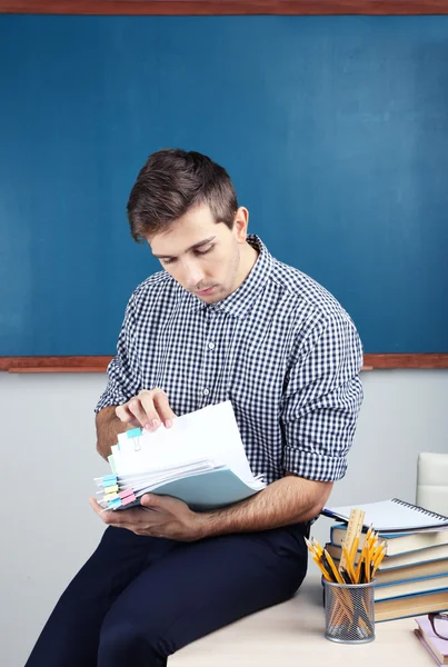 Young teacher sitting on desk in school classroom — Stock Photo, Image