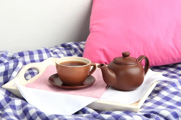 Cup and teapot on wooden tray on bed on wall background — Stock Photo, Image