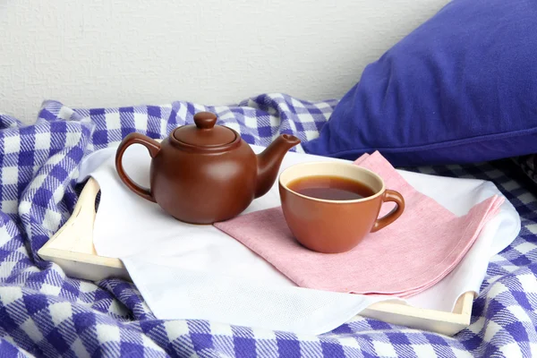 Tasse und Teekanne auf Holztablett auf Bett auf Wandhintergrund — Stockfoto