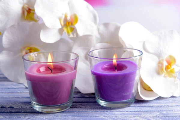 Belle candele colorate e fiori di orchidea, sul tavolo di legno a colori, su sfondo chiaro — Foto Stock