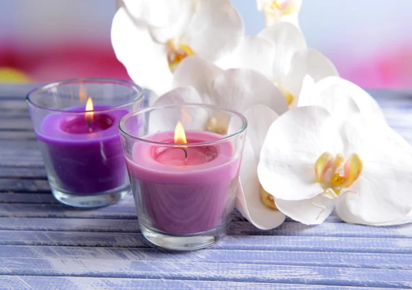 Belle candele colorate e fiori di orchidea, sul tavolo di legno a colori, su sfondo chiaro — Foto Stock