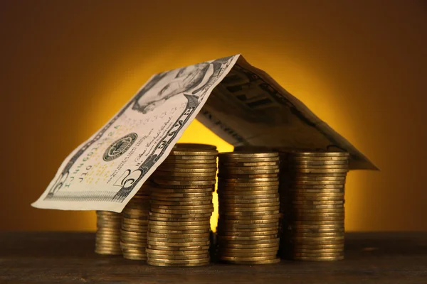 Monedas casa en la mesa sobre fondo marrón — Foto de Stock