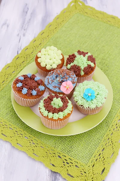 Tasty cupcakes with butter cream, on plate, on color napkin, on color wooden background