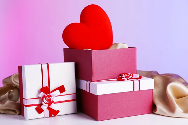 Stack of gift boxes and decorative heart, on color background — Stock Photo, Image